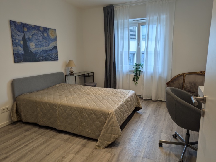 Blick ins Zimmer mit Doppelbett, Fenster, Sofa und Arbeitsplatz