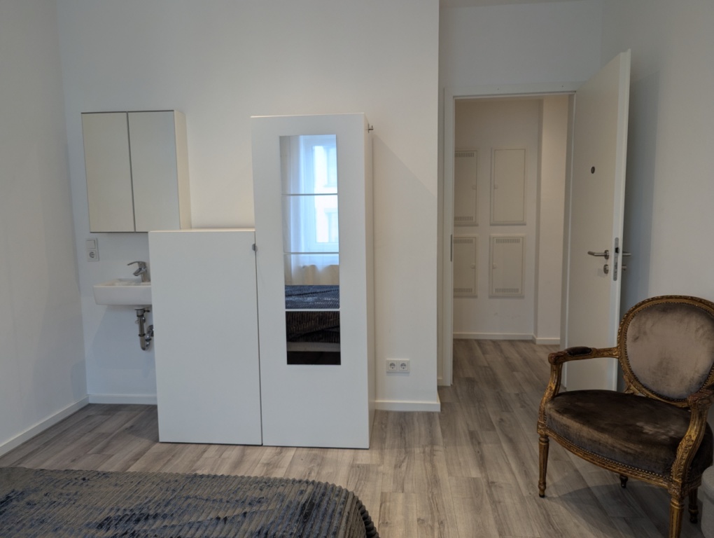 WG-Zimmer Innenstadt An der Staufenmauer 11 - Blick vom Doppelbett auf Waschbecken im Zimmer, Kleiderschrank, Tür und Lesestuhl